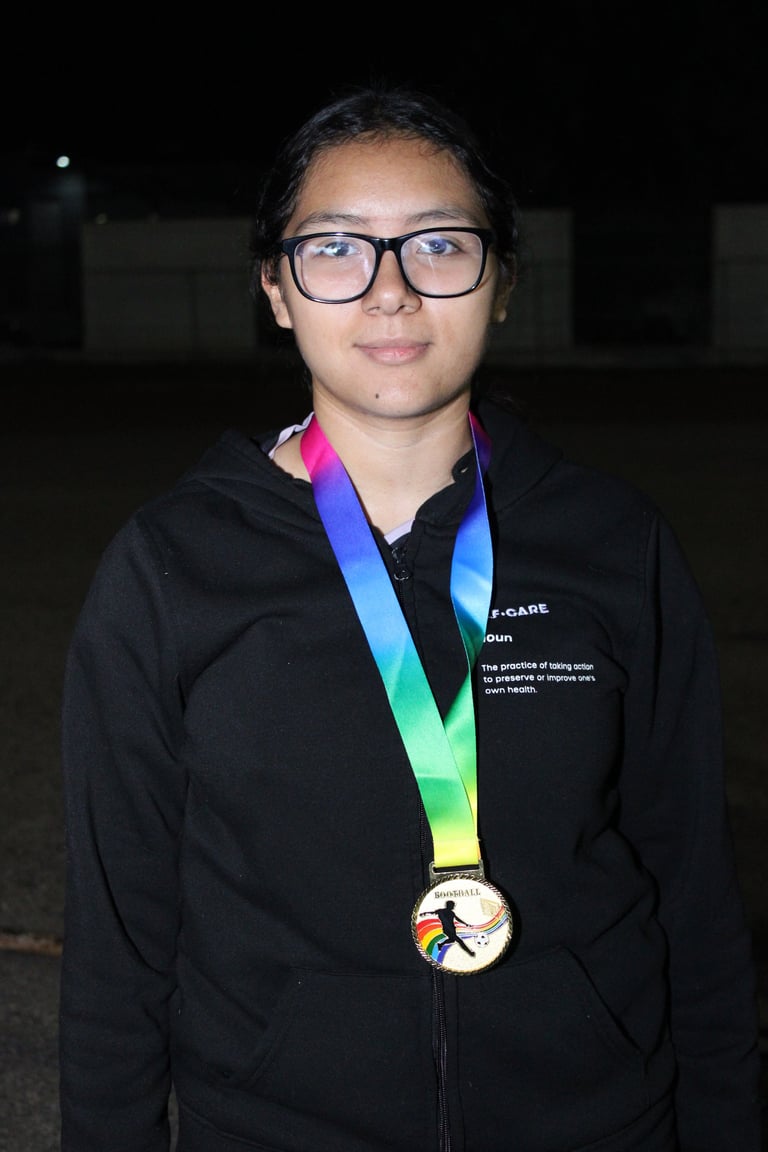 Young person wearing glasses and a black jacket with a colorful rainbow medal on a lanyard