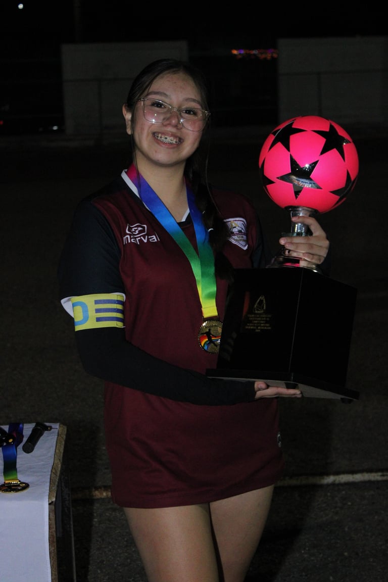Young woman in maroon sports jersey holding illuminated soccer ball trophy and wearing medal around neck