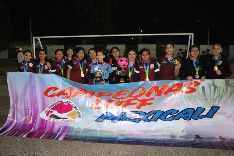 Girls soccer team holding championship banner at night on field, wearing medals and team uniforms