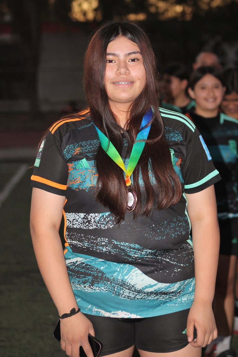 Young woman wearing a black and turquoise sports jersey with rainbow medal, standing outdoors at an event