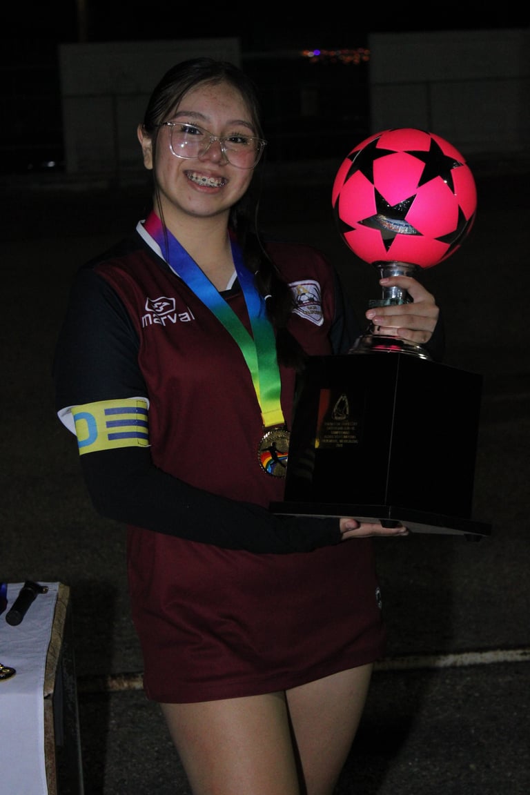Smiling young athlete holding a glowing soccer ball trophy while wearing a maroon sports uniform and medal