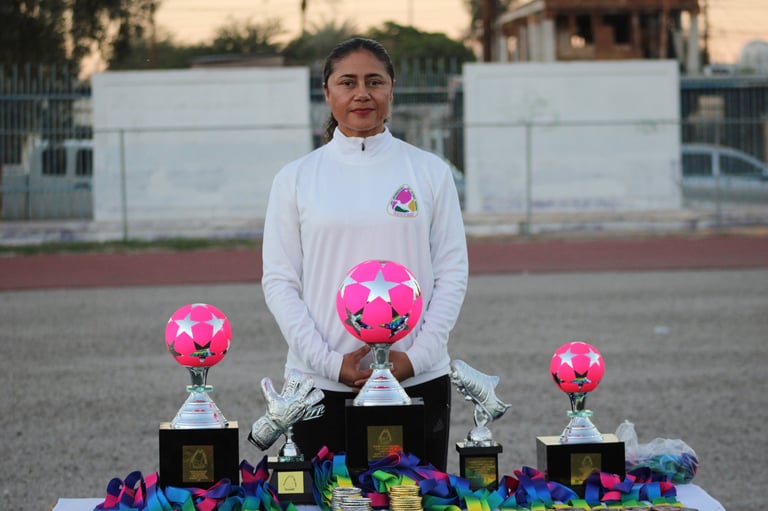Young athlete holding pink soccer ball trophies at sports award ceremony display table outdoors
