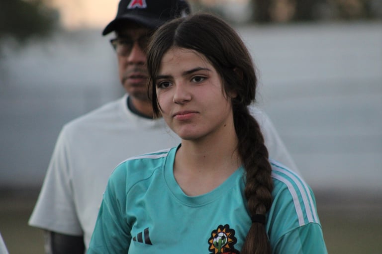 Young woman with dark braided hair wearing a turquoise Adidas athletic shirt, with a man in a cap visible in the background