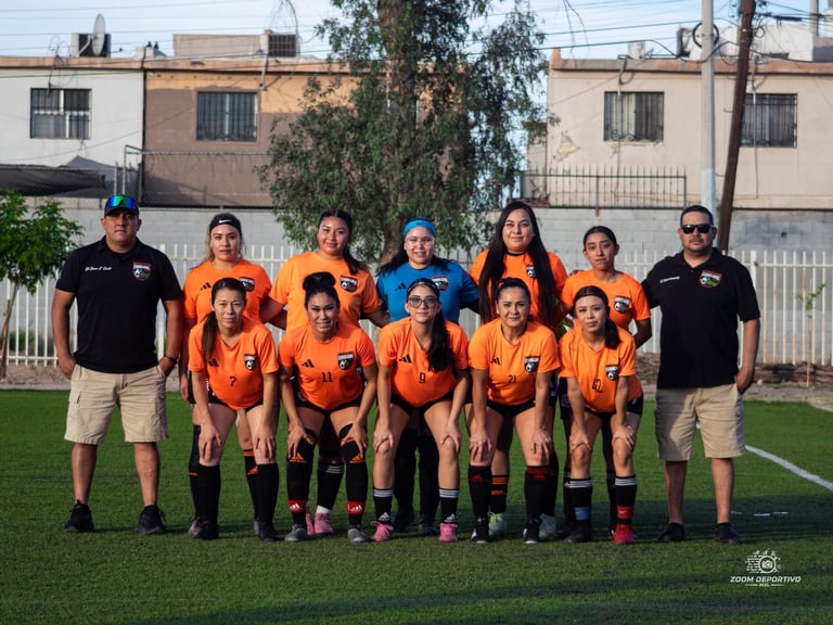 Youth soccer team in orange uniforms with coaches posing on grass field in front of residential buildings