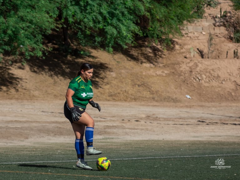 Soccer player in green jersey dribbling yellow ball on artificial field with sandy hill background