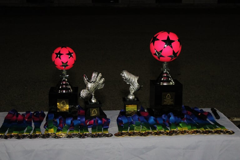 Two pink soccer trophies with miniature team figurines lined up below them on a reflective surface against a black background