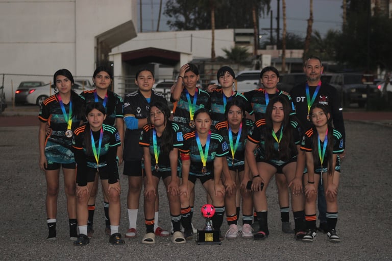 Youth sports team in black uniforms and medal ribbons posing together outdoors in a parking lot