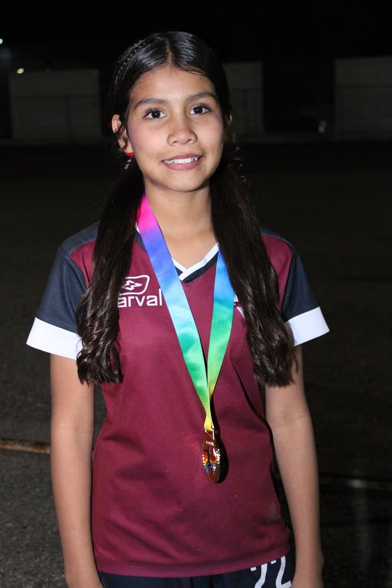 Young girl wearing maroon sports jersey with white stripes and colorful medal around neck, smiling at camera