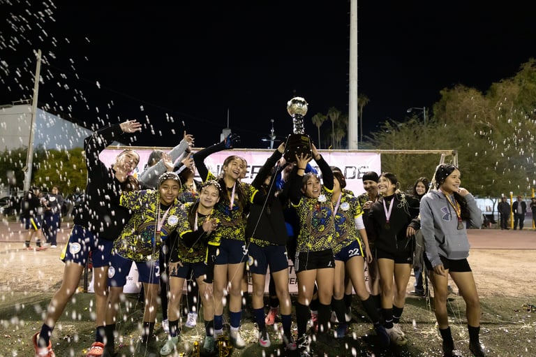 Sports team celebrating with champagne spray at night, holding trophy under stadium lights after winning championship game