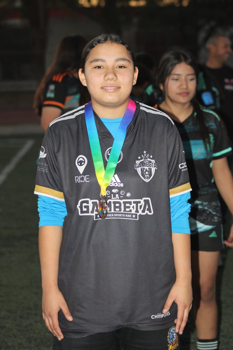 Young athlete wearing black sports jersey with rainbow medal around neck, smiling at camera with teammates in background