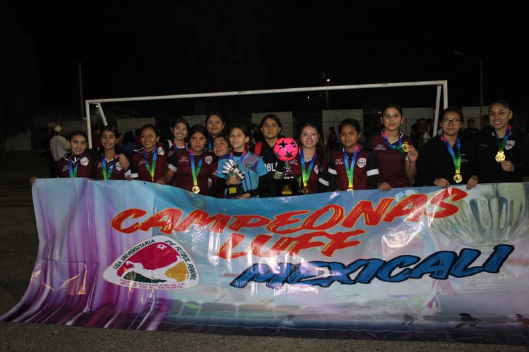 Youth soccer team holding a championship banner, wearing medals and dark uniforms, posing together at night
