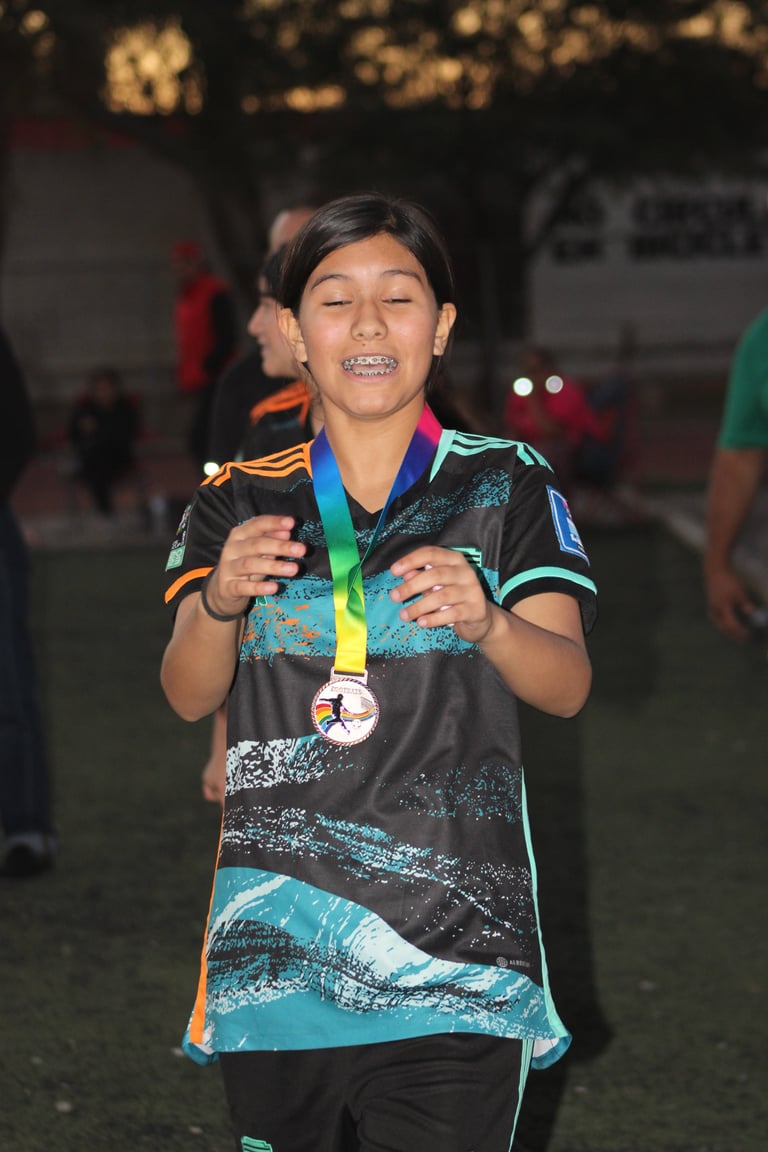 Young athlete smiling while wearing a turquoise and black sports jersey with a green medal around their neck at an outdoor event