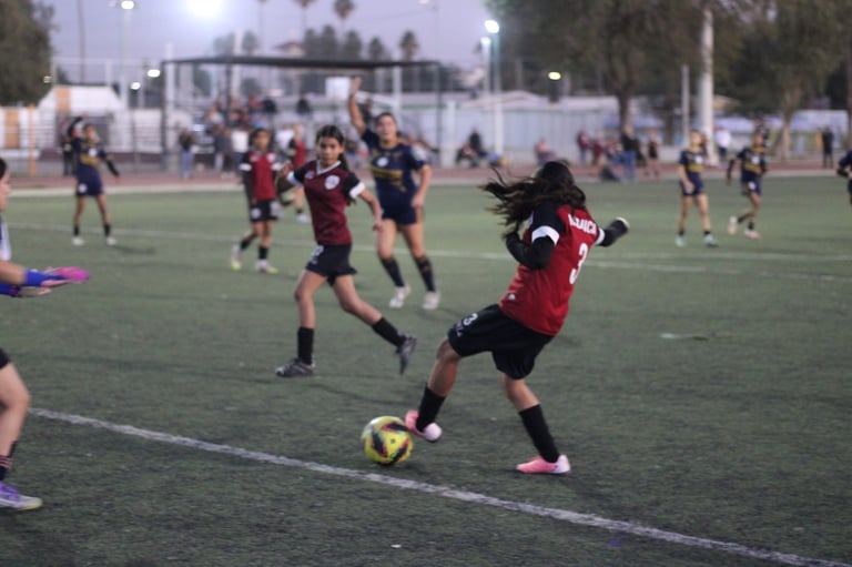 Young soccer player in dark red jersey controlling ball during evening match on grass field with other players in background