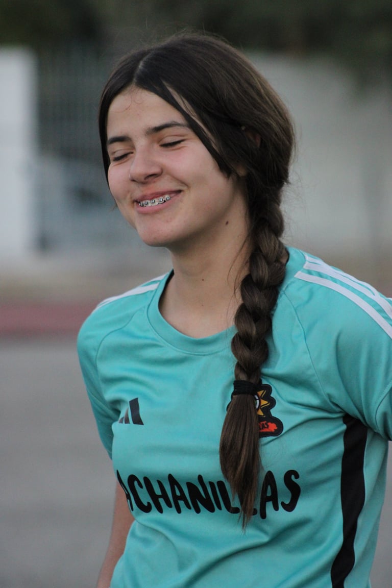 Young woman with braided dark hair smiling, wearing a turquoise sports jersey with white stripes, outdoors