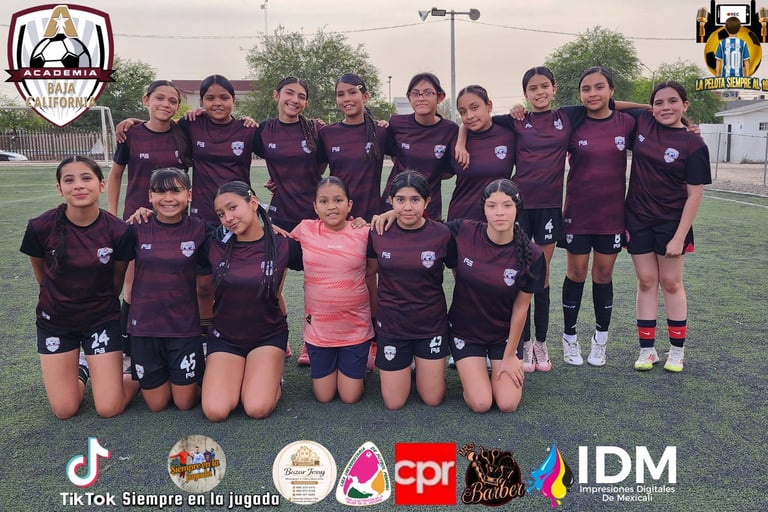 Female youth soccer team in maroon uniforms posing for a team photo on a grass field with sponsor logos visible