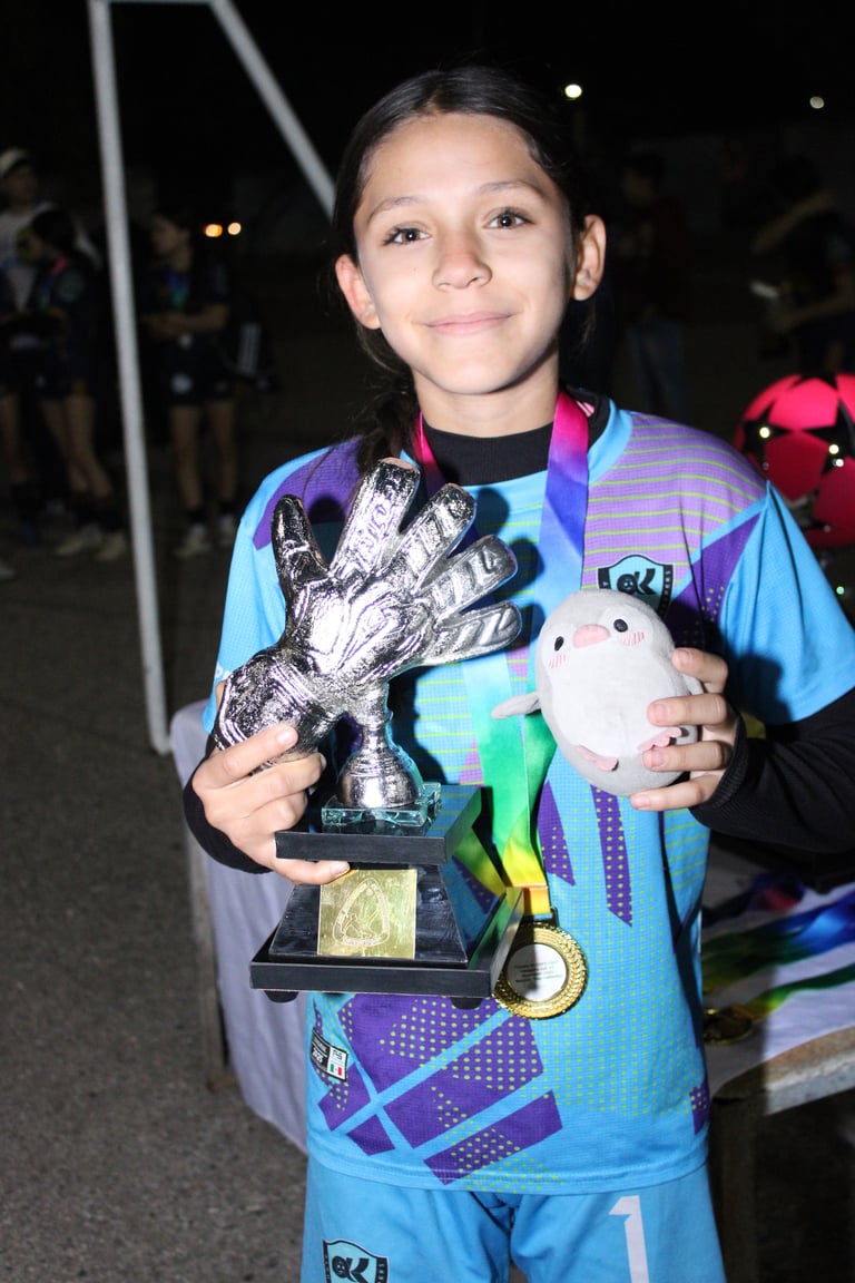 Young soccer player holding a trophy and medal at night event, wearing blue and purple striped jersey