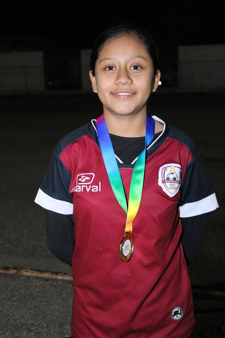 Young athlete wearing maroon and navy sports jersey with rainbow medal around neck, smiling at camera
