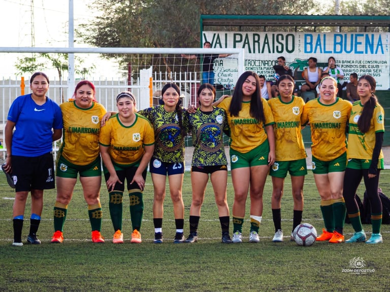 Womens soccer team in yellow and green uniforms lined up on field with coach in blue