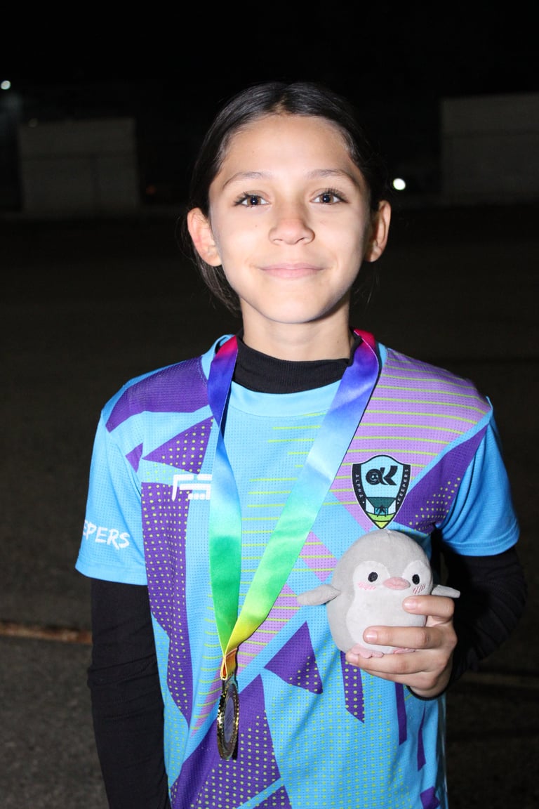 Young child wearing colorful athletic shirt and rainbow medal, holding small plush toy, smiling at camera