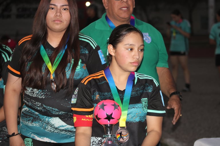 Young athletes wearing medals and team uniforms stand together at a sports event, with one holding a pink trophy ball