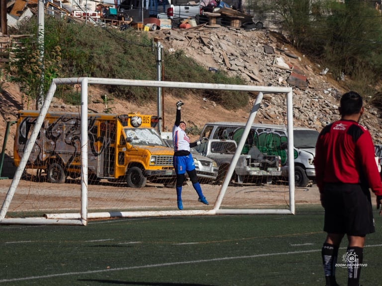 Soccer player in blue jersey about to kick ball toward goal, with vehicles and construction site visible in background