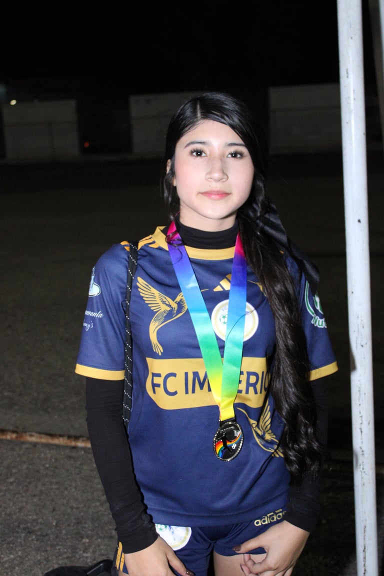 Young athlete wearing navy and gold sports uniform with medal around neck, standing indoors at night