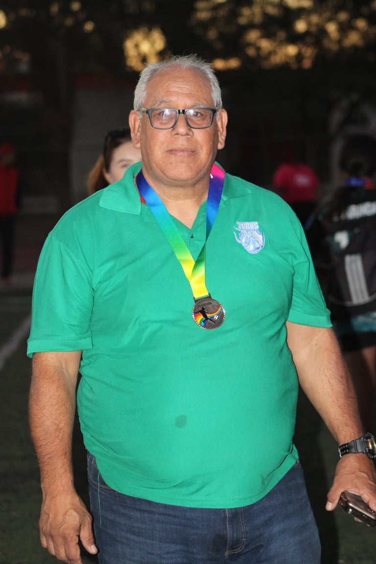 Older man wearing glasses and a green polo shirt with a medal on a ribbon around his neck at an indoor event