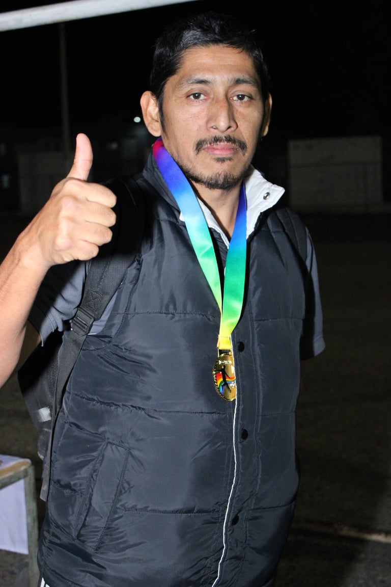 Man in black jacket with rainbow medal giving thumbs up gesture at night event