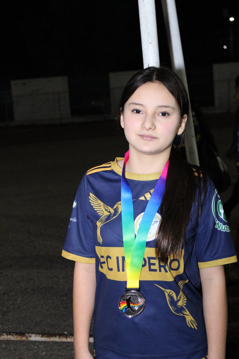 Young girl wearing navy blue sports jersey with gold trim and colorful medal around neck, standing outdoors at night
