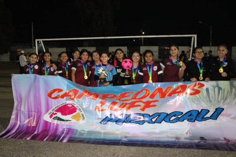 Group of young athletes wearing medals standing behind a colorful banner at a nighttime sports event celebration