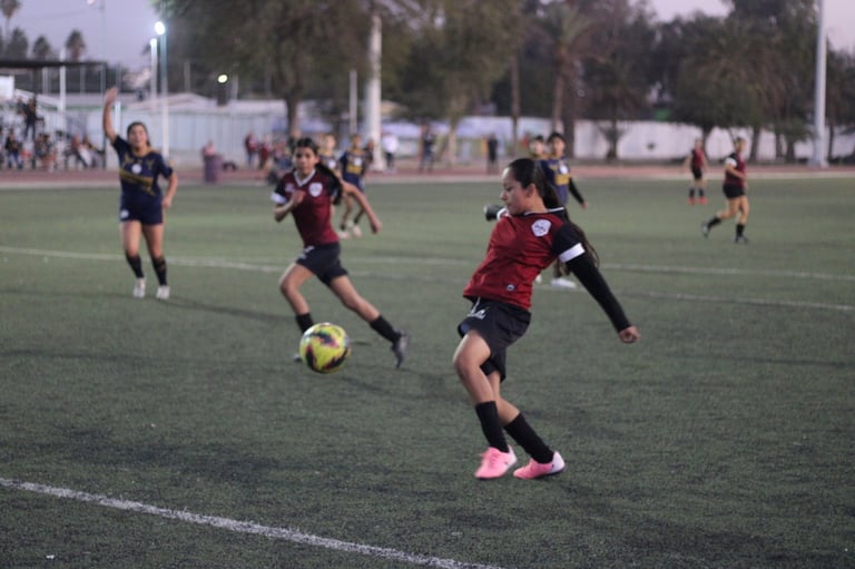 Youth soccer players in red and black uniforms compete for the ball on a grass field during a match
