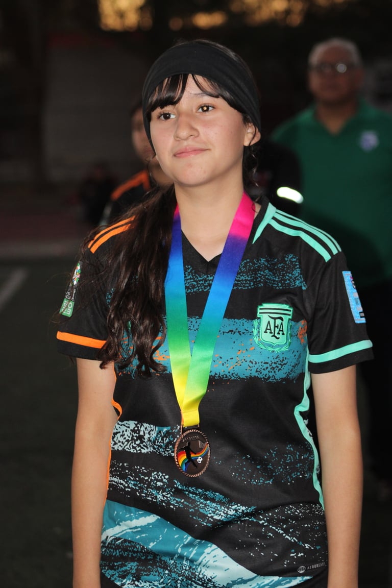 Young girl wearing colorful Argentine sports jersey and rainbow medal around her neck at an indoor event