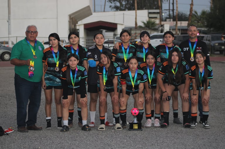 Youth soccer team in dark uniforms with medals poses for a group photo with coaches outdoors