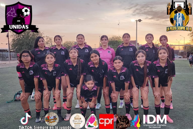 Youth girls soccer team in dark jerseys posing on field at sunset with sponsor logos and team branding