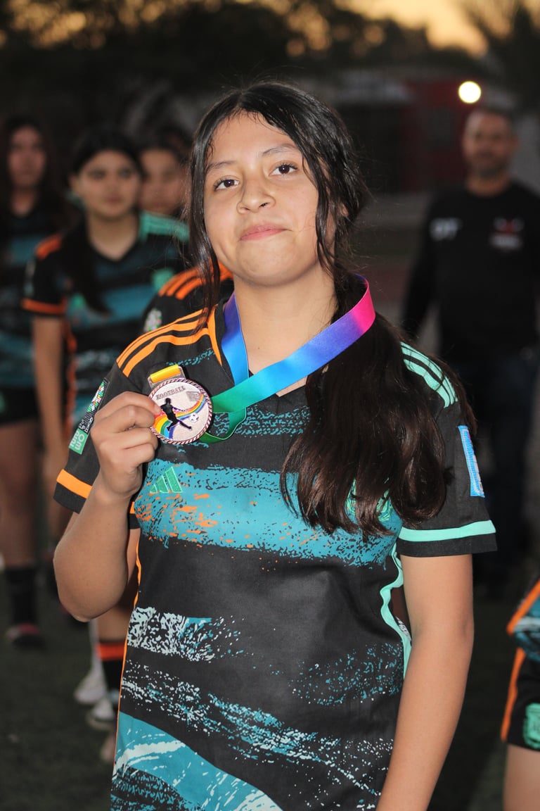 Young athlete holding up a medal on a colorful ribbon at an outdoor sports event