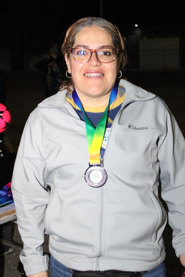 Woman wearing glasses and Columbia jacket smiling at camera while displaying a medal on blue and yellow ribbon