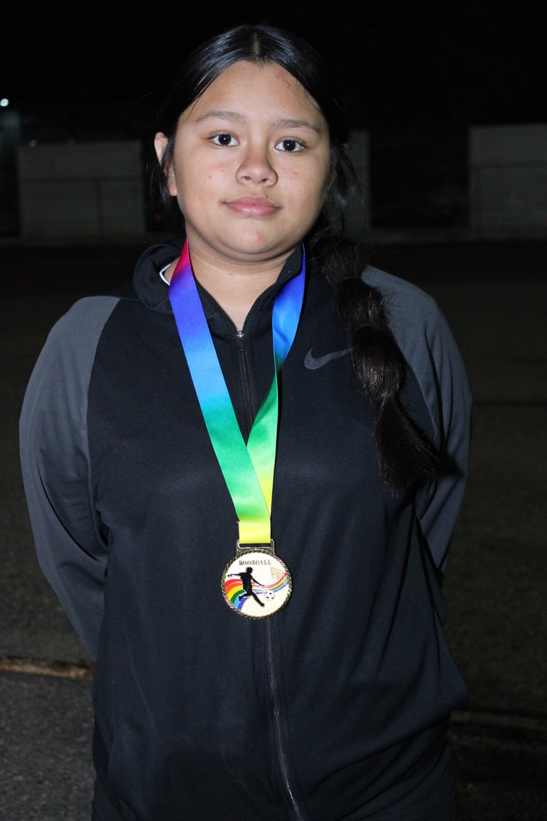 Young person wearing a black Nike jacket and a colorful ribbon medal, standing against a dark background at night