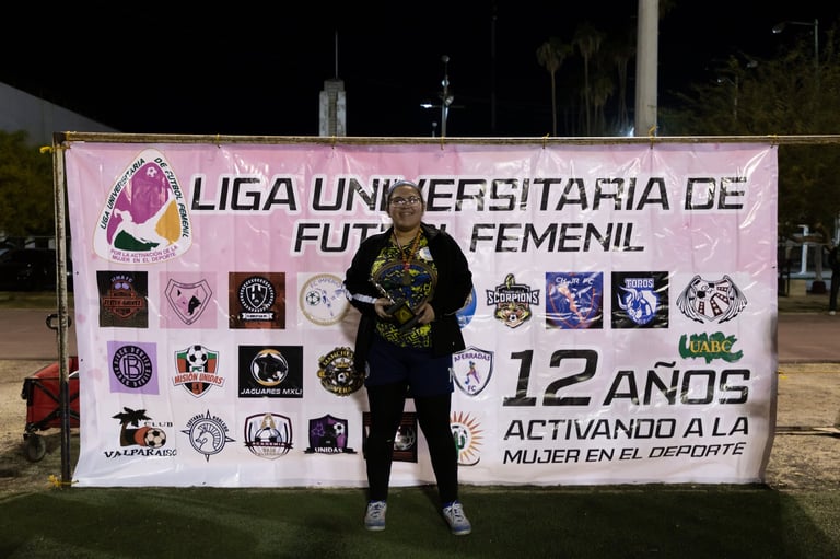 Woman standing in front of pink Liga Universitaria de Futbol Femenil banner at night on grass field