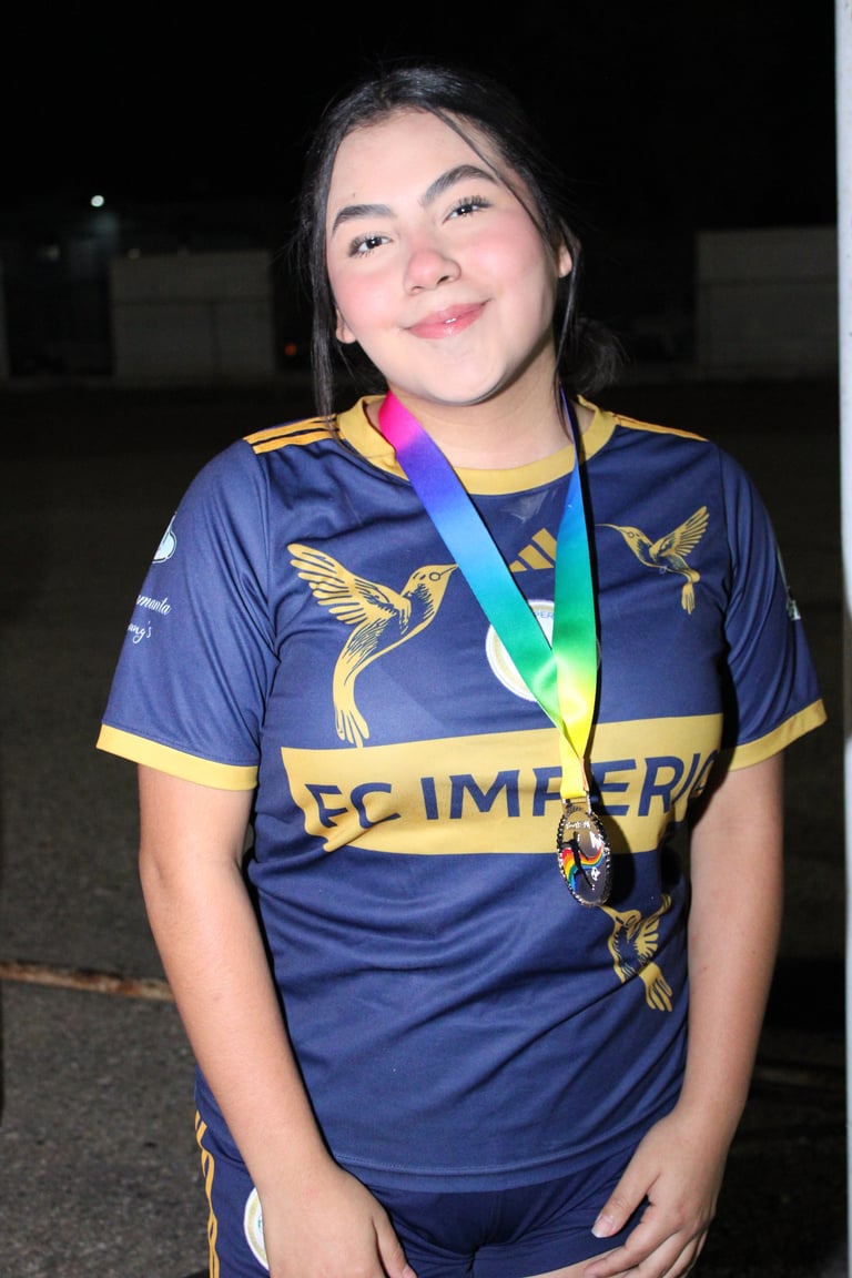 Young female athlete wearing navy and gold sports jersey with medal around neck, smiling at camera outdoors at night