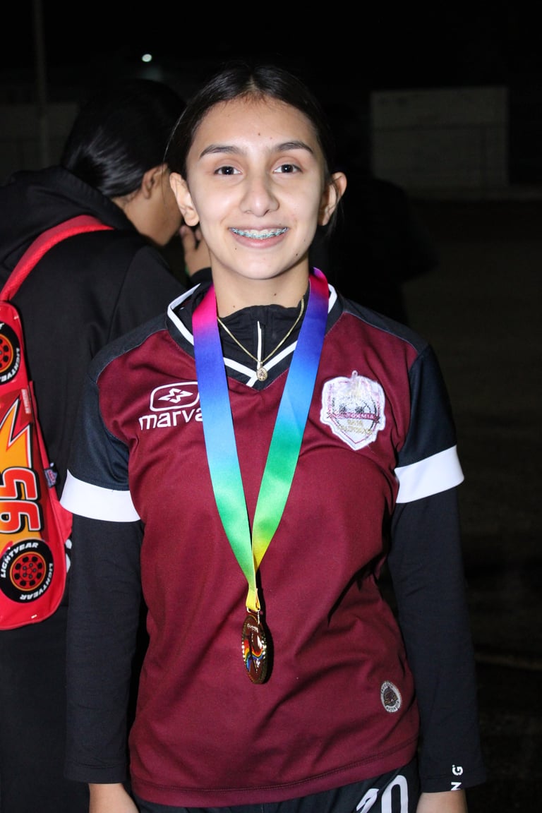 Young athlete smiling while wearing maroon team jersey and rainbow medal around neck