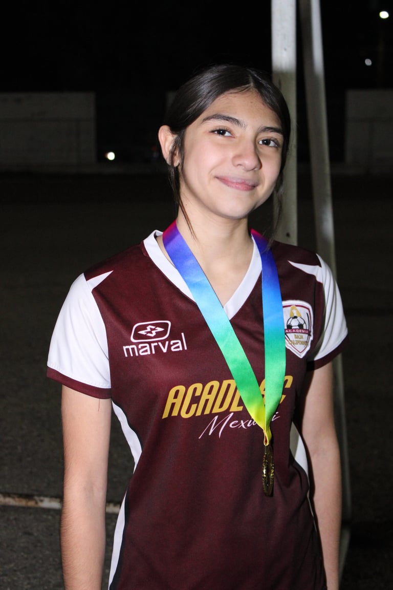 Young athlete in maroon and white soccer jersey wearing a blue and green medal around her neck, smiling at camera
