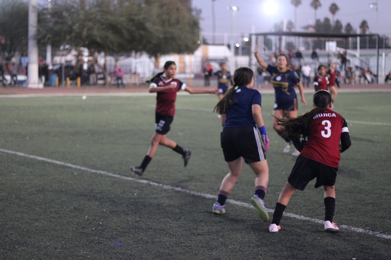 Youth soccer players in maroon and navy uniforms playing on a field with spectators in the background