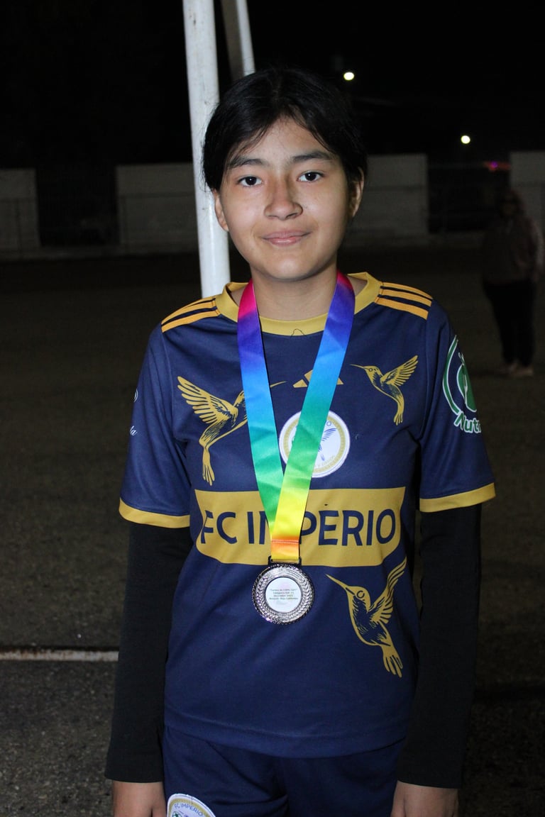 Young athlete wearing dark athletic jersey with gold trim, displaying a rainbow medal around neck at night