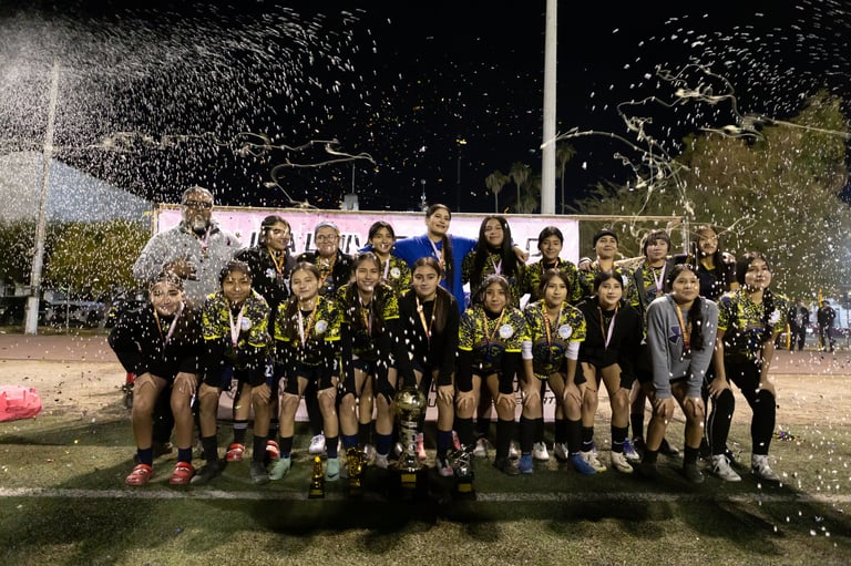 Youth soccer team in black and yellow uniforms celebrating with confetti at night on a grass field