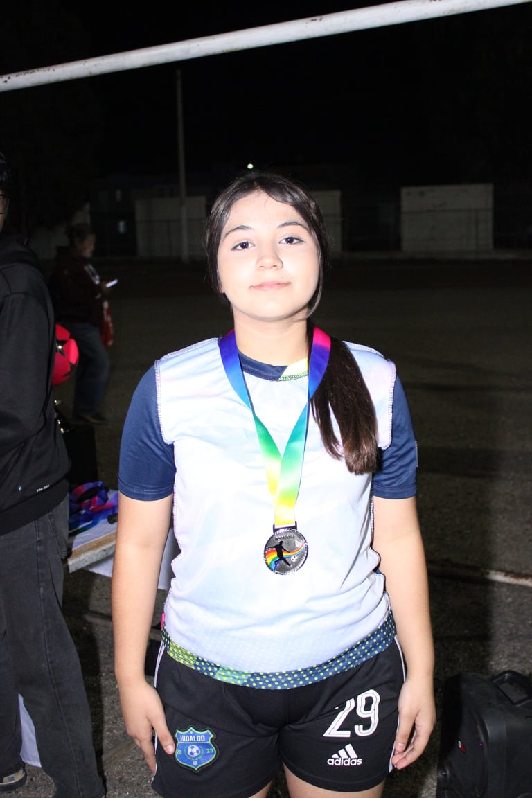 Young athlete in sports uniform wearing medal around neck, standing at night on a court or field