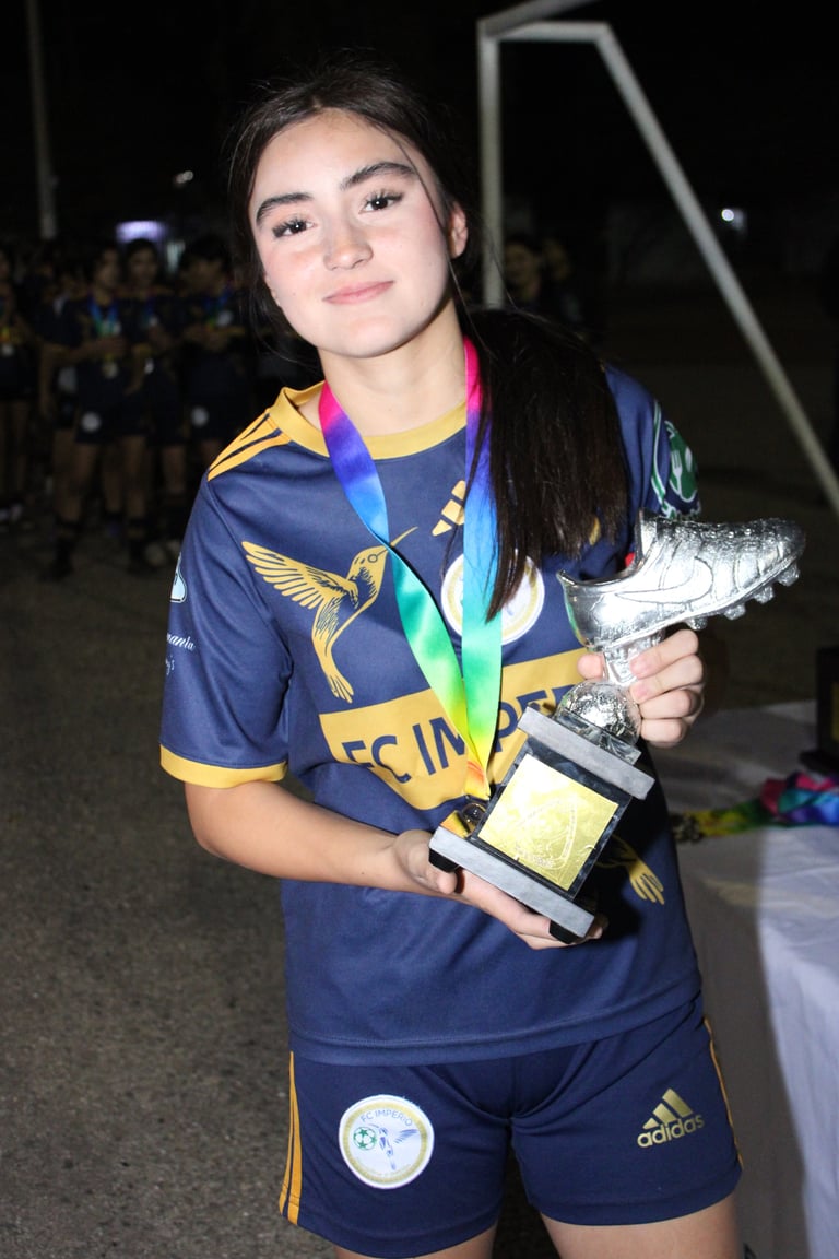 Young athlete in navy sports uniform holding trophy and wearing rainbow medal around neck at nighttime event