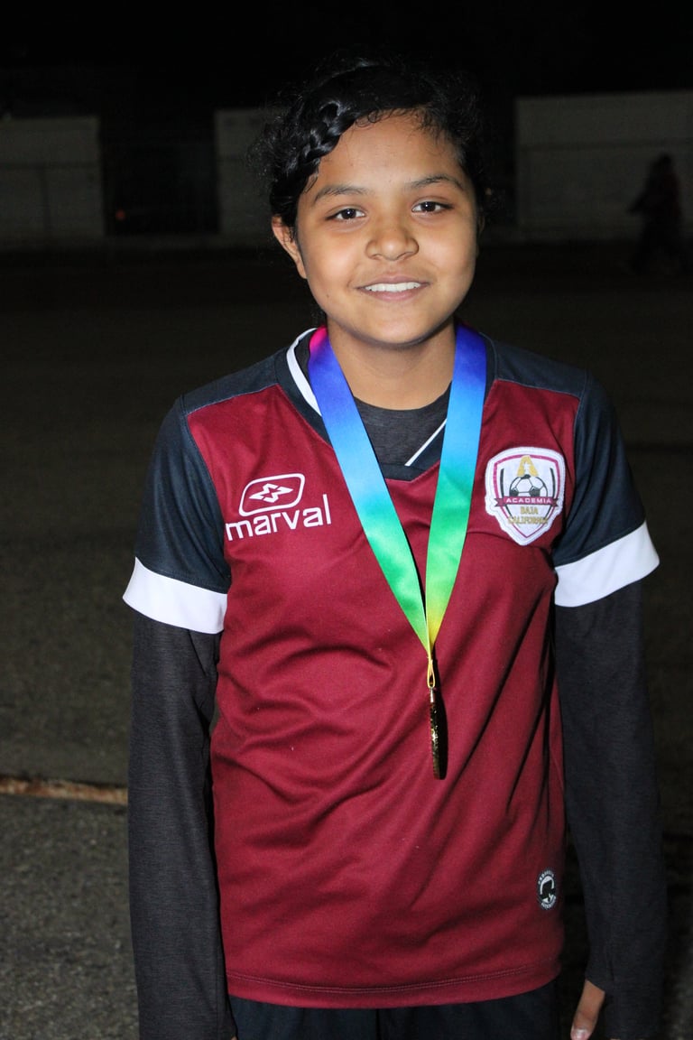 Young athlete wearing maroon and black sports jersey with medal around neck, smiling at camera against indoor background