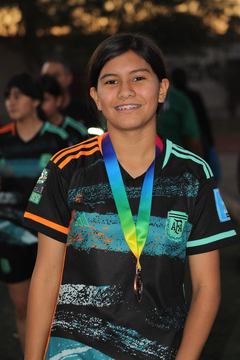 Young athlete smiling while wearing a colorful sports jersey and blue medal around neck at an outdoor event