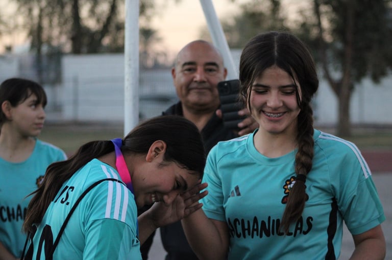 Group of young soccer players in turquoise uniforms smiling with coach at outdoor sports field