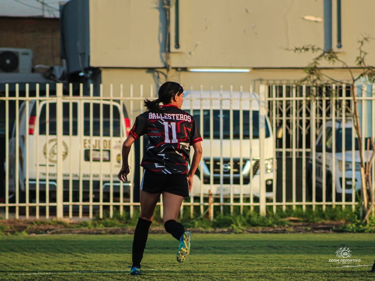 Soccer player wearing burgundy jersey number 11 running on grass field with yellow gate in background